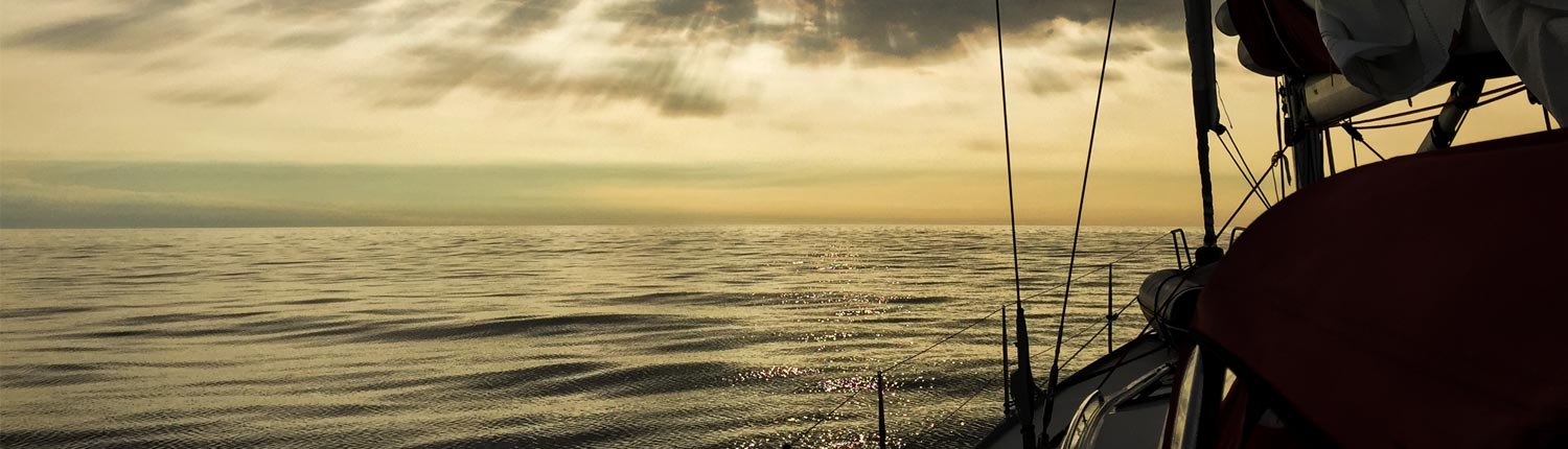 Blick von einem Segelboot auf das offene Meer. Der Himmel ist mit Wolken bedeckt und die Sonne scheint warmweiß durch sie hindurch.